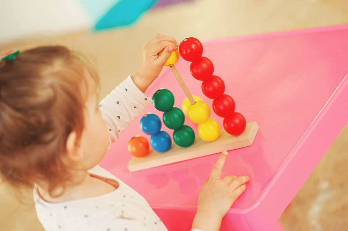 Daycare overnight care little cheerful girl playing with colorful wooden construction blocks at home, in kindergarten or preschool. Creative games for kids. Family education concepts